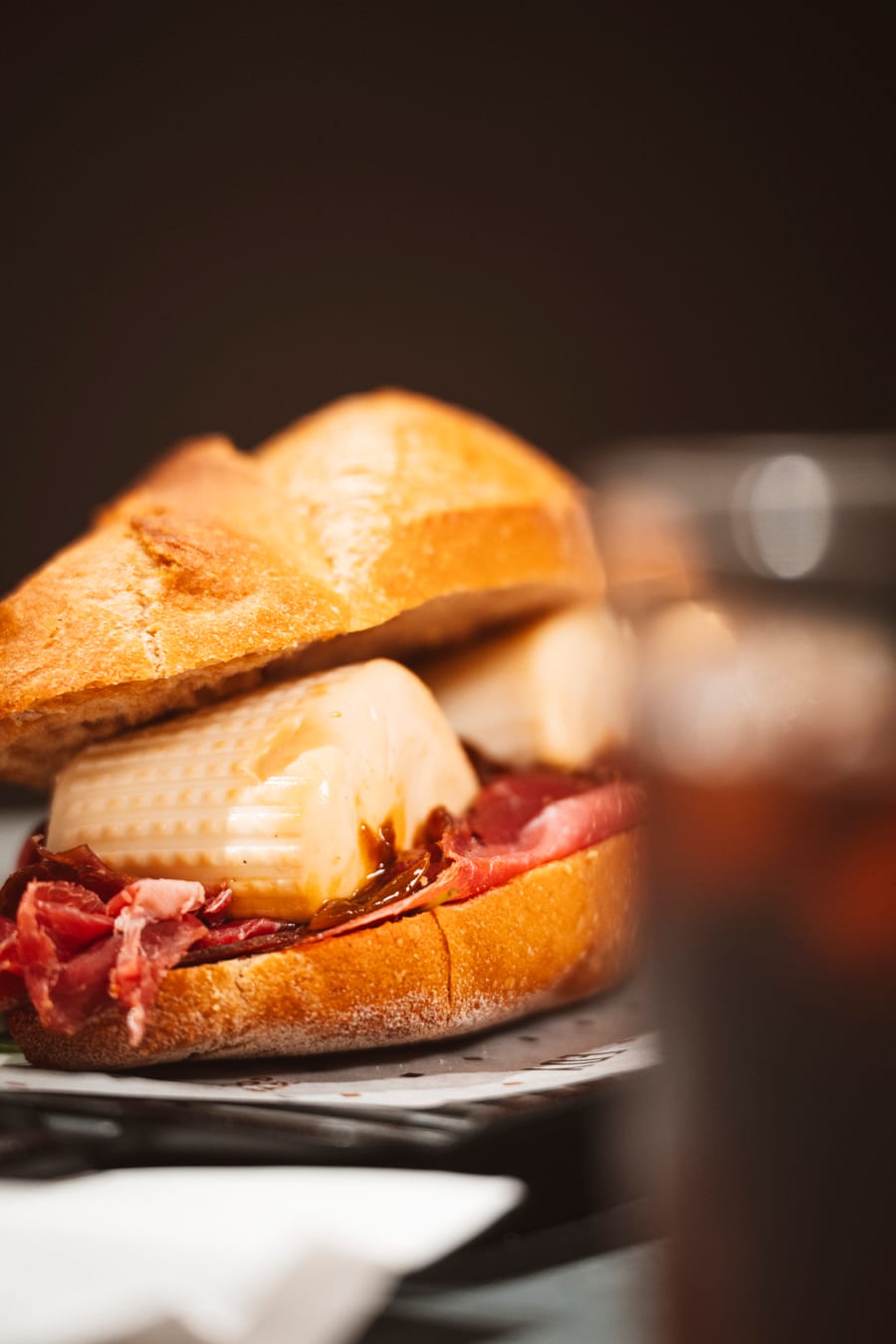 Primo piano del panino col crudo e la burrata, controluce sul fondo scuro