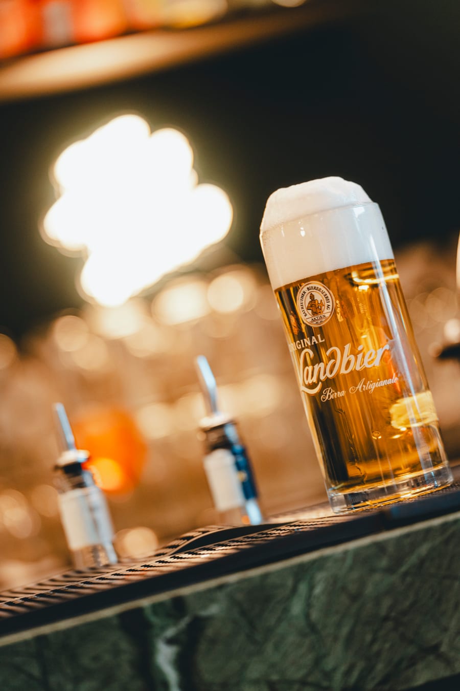 Un boccale di birra appena spillata sul banco di marmo verde, davanti alle luci del bar