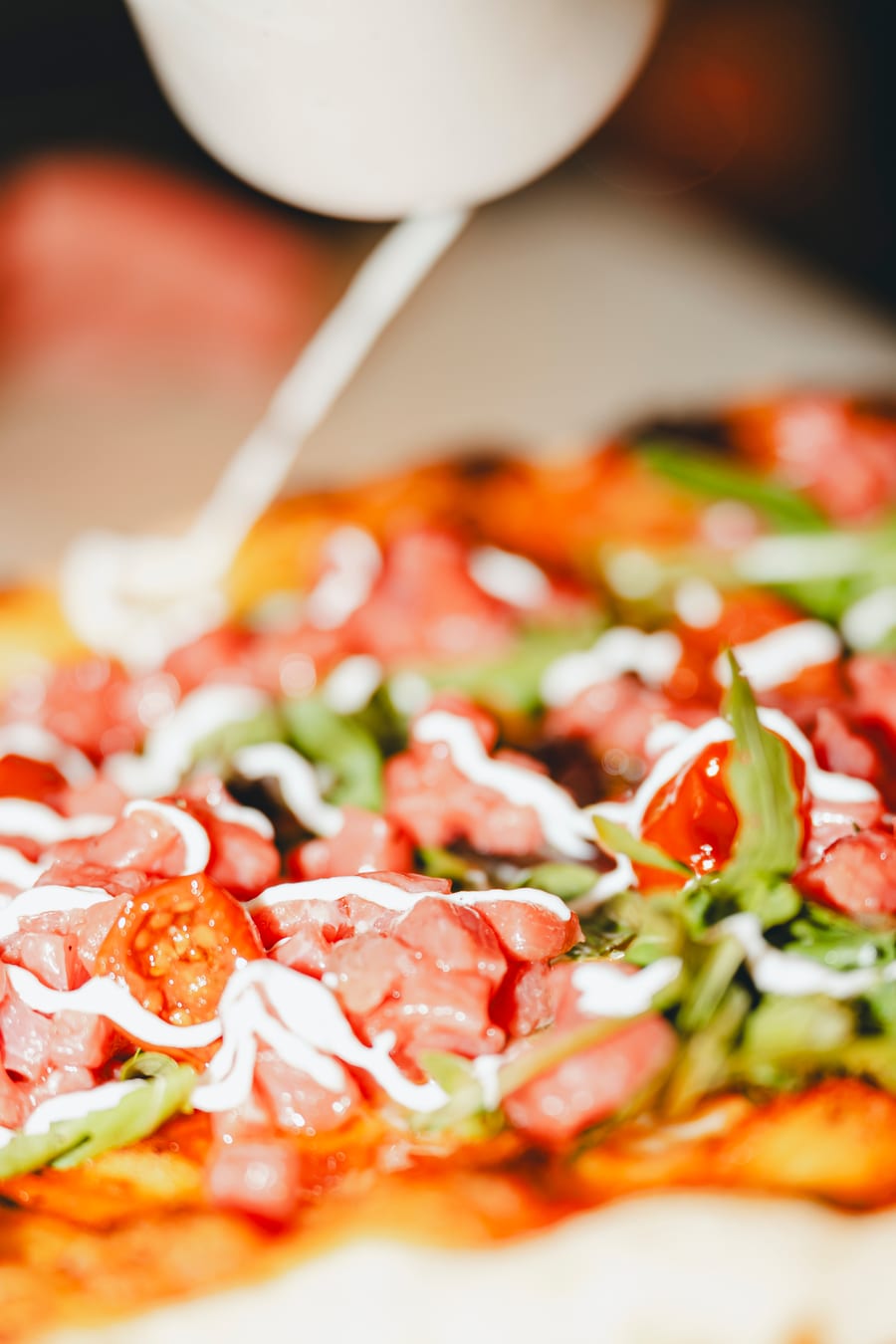 Una pizza con la tartare, la rucola e un filo di salsa bianca che cade dall’alto