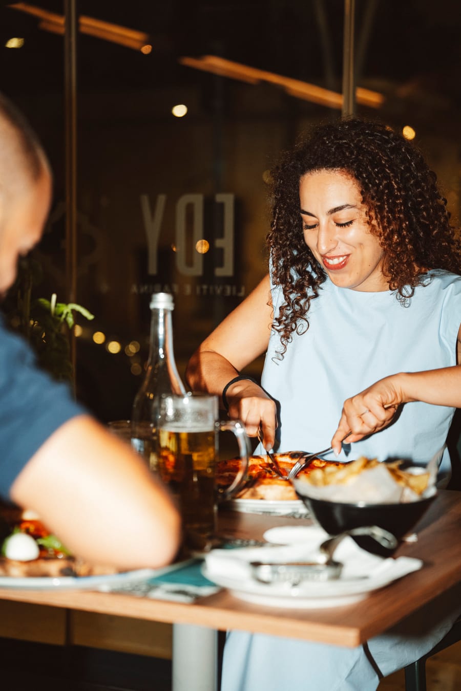 Una cliente si serve al tavolo, la sera, dietro il vetro con il marchio del locale