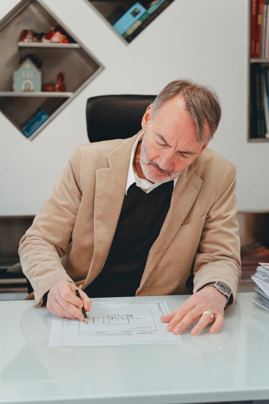 Il collega firma un documento alla scrivania, giacca beige sul maglione scuro