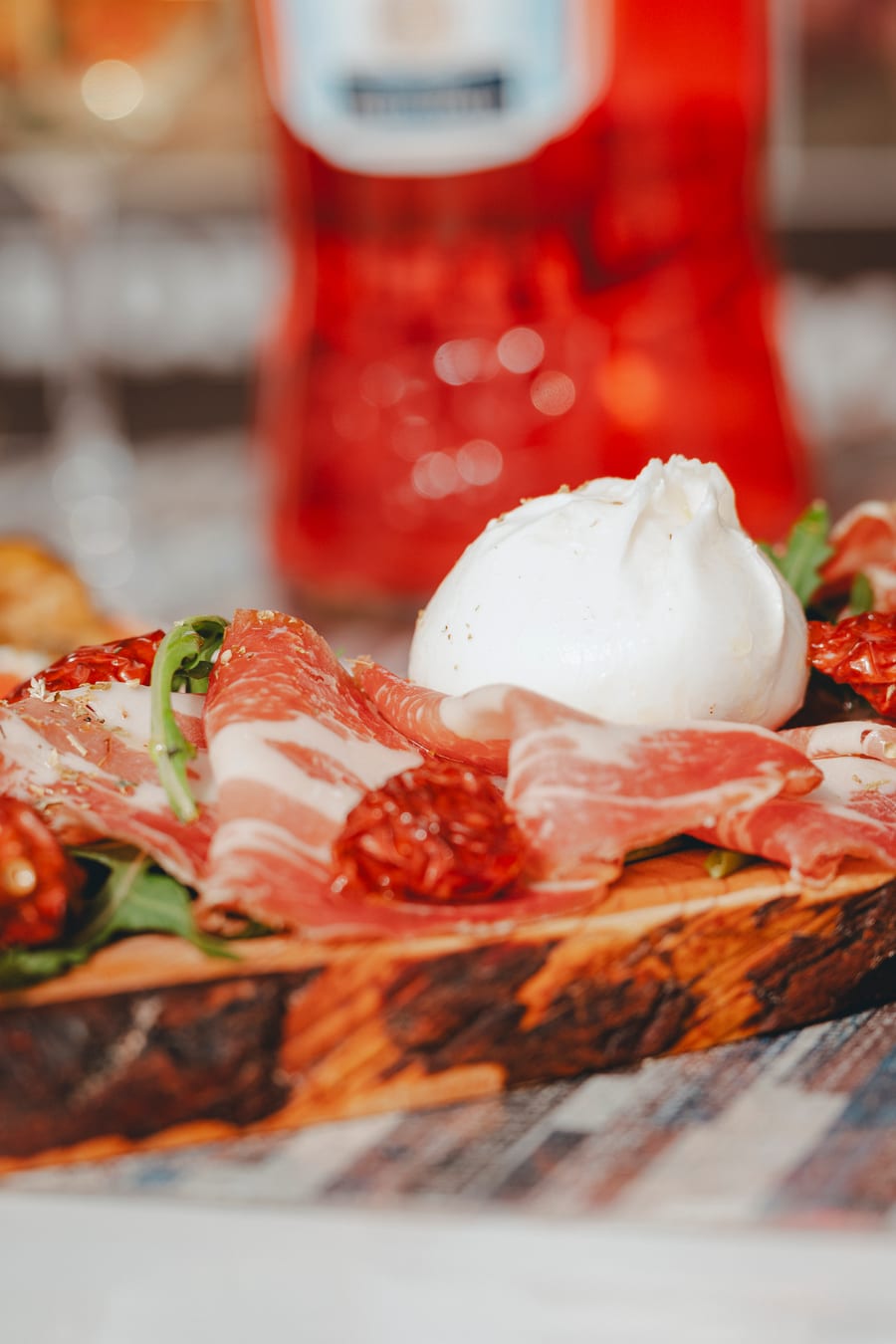 Tagliere di prosciutto, salame e burrata, con uno spritz sullo sfondo