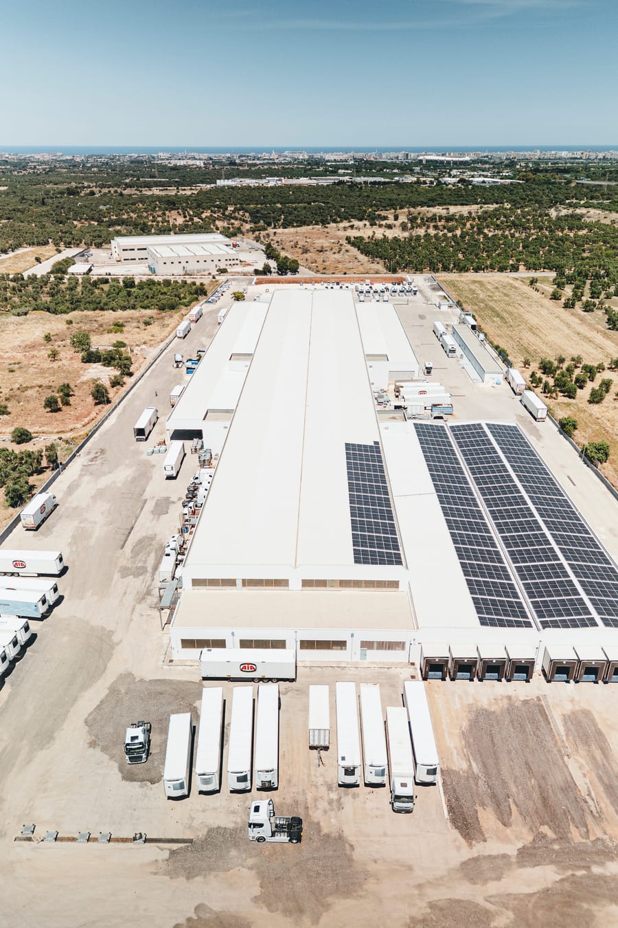 La piattaforma logistica vista dal drone, i semirimorchi allineati alle baie di carico e i pannelli solari sul tetto