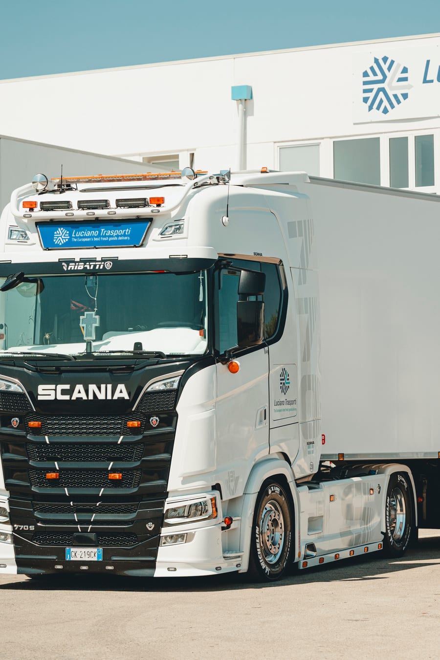 Il muso nero di uno Scania agganciato al semirimorchio frigo in livrea, davanti all’insegna della sede