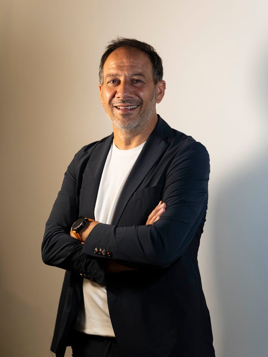 Ritratto in studio: giacca scura sopra la maglietta bianca, braccia incrociate, sorriso