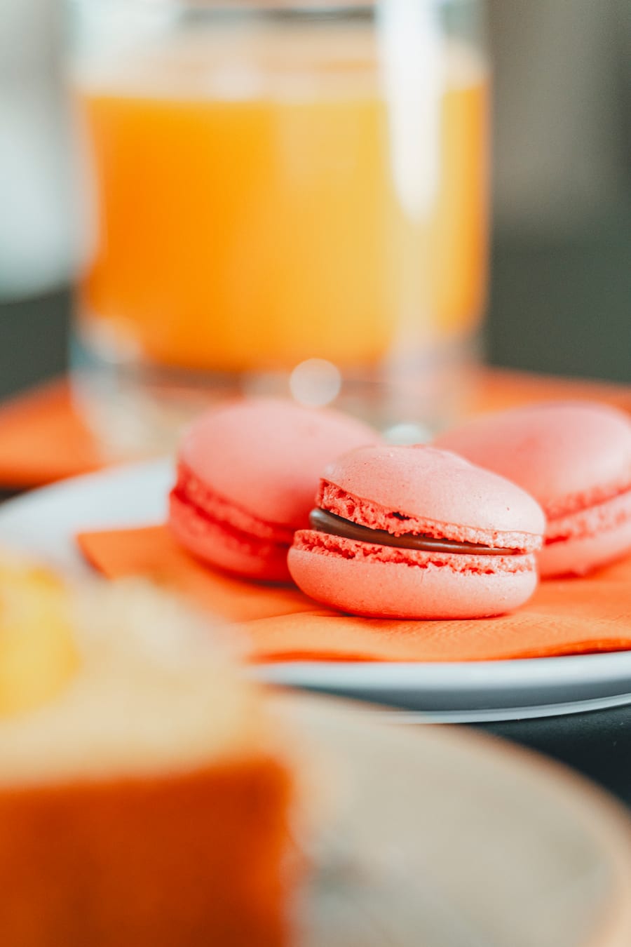 Due macaron rosa su un tovagliolo arancione, accanto ai bicchieri di succo