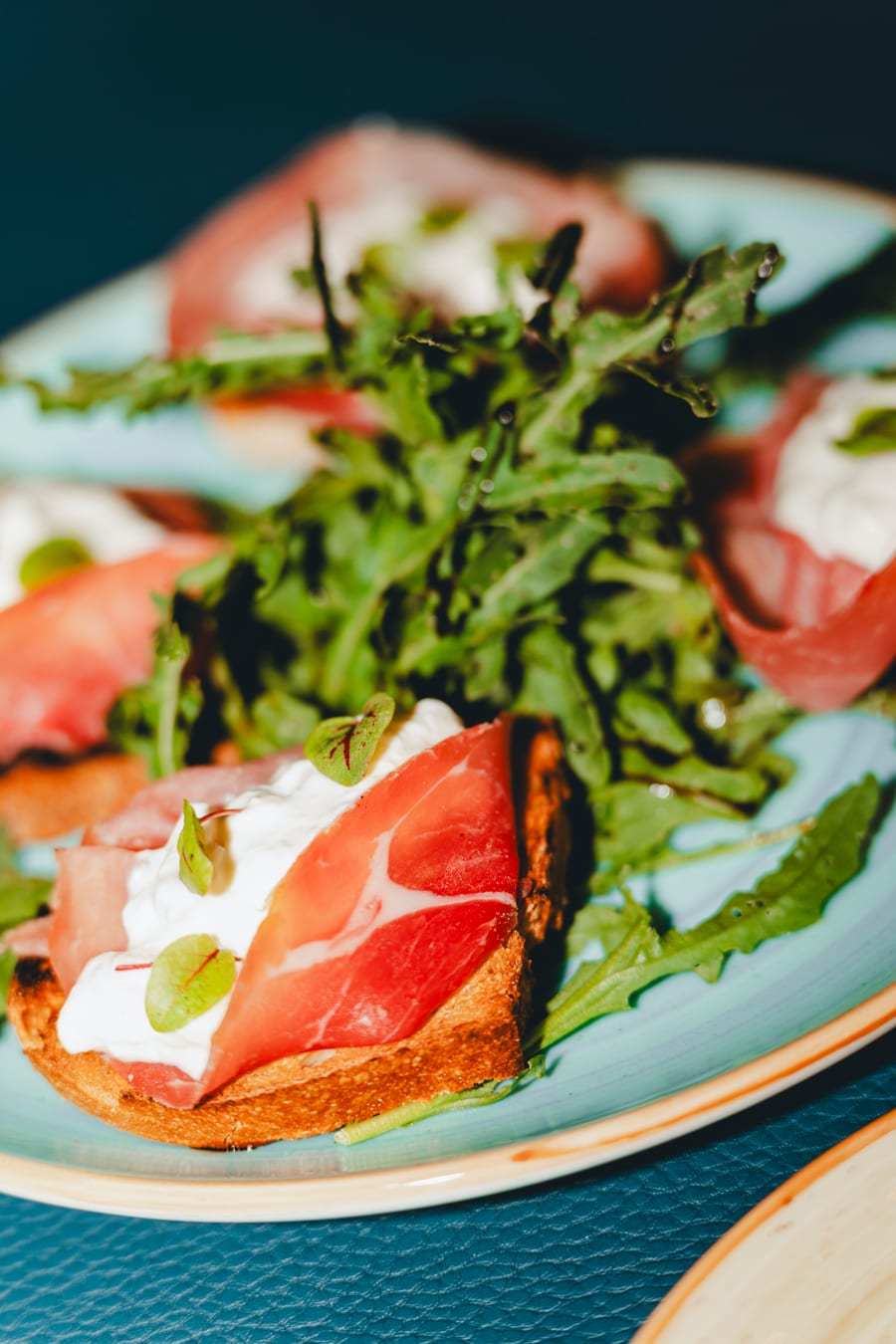Una bruschetta con crudo, burrata e rucola servita nel piatto